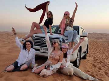 Group of Young Tourist Girls sitting on Landcruiser & Sand during Morning Safari Tour in Dubai Desert